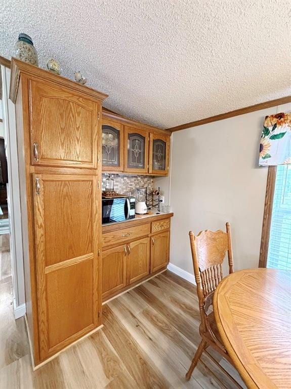 dining area with bar area, ornamental molding, a textured ceiling, and light wood-style flooring