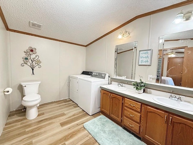 ensuite bathroom featuring a textured ceiling, washing machine and clothes dryer, a sink, visible vents, and ornamental molding