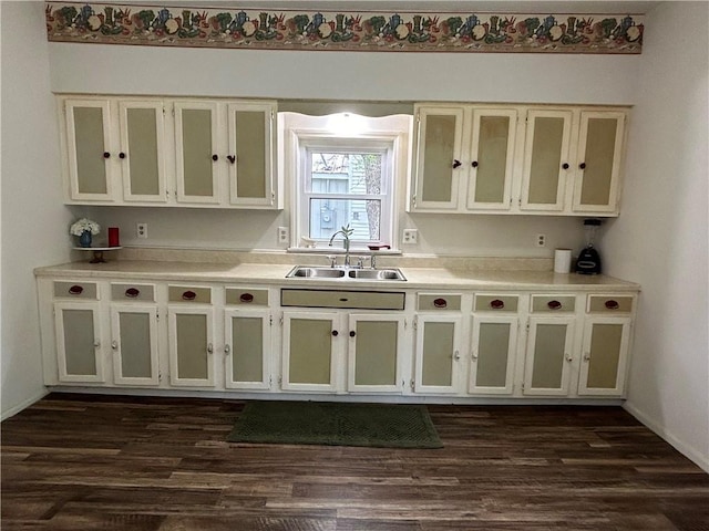 kitchen featuring dark wood finished floors, glass insert cabinets, light countertops, and a sink