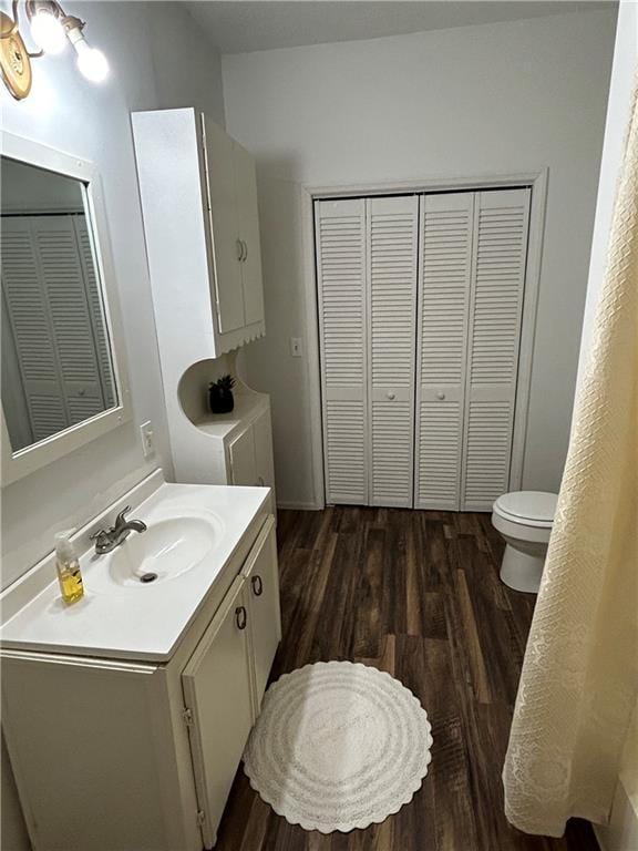 bathroom with wood finished floors, toilet, vanity, and a closet