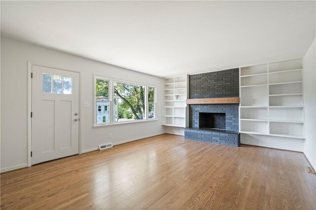 unfurnished living room with visible vents, a brick fireplace, built in shelves, wood finished floors, and baseboards