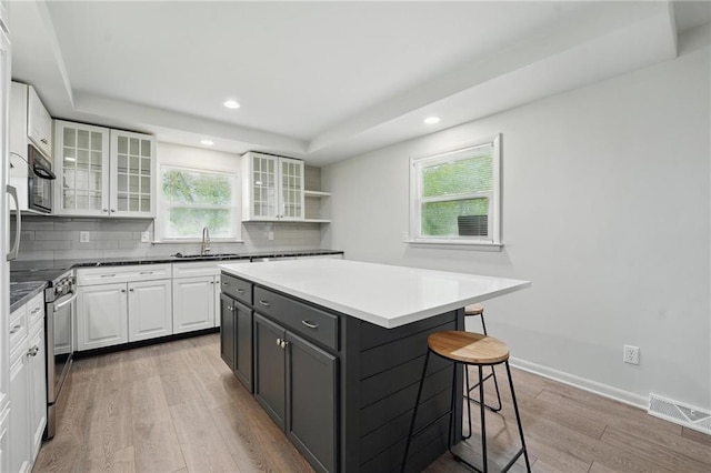 kitchen with white cabinets, stainless steel range with electric stovetop, a kitchen breakfast bar, light wood-type flooring, and a tray ceiling