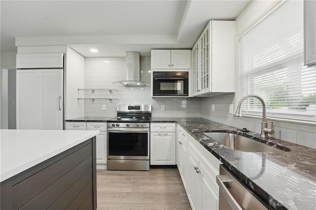 kitchen featuring wall chimney range hood, white cabinetry, a sink, backsplash, and stainless steel appliances