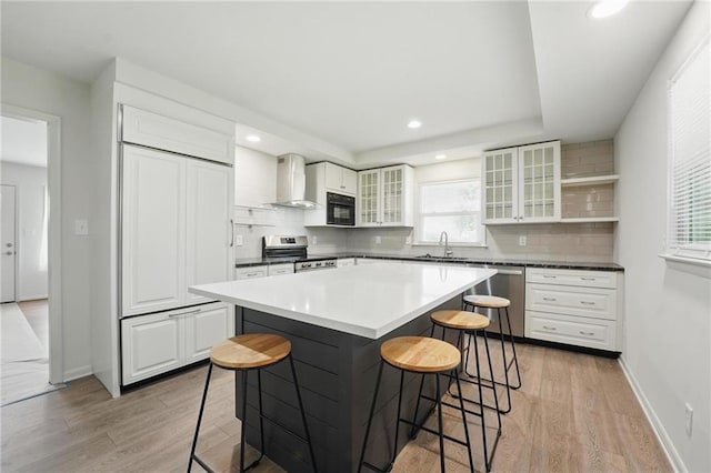 kitchen featuring appliances with stainless steel finishes, a breakfast bar, a sink, wall chimney exhaust hood, and light wood-type flooring