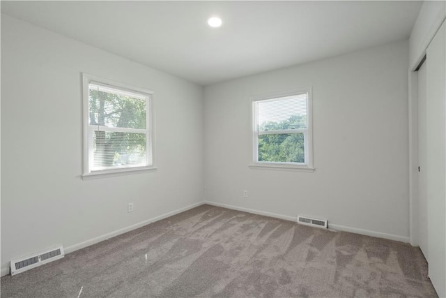 carpeted spare room featuring visible vents, baseboards, and a wealth of natural light
