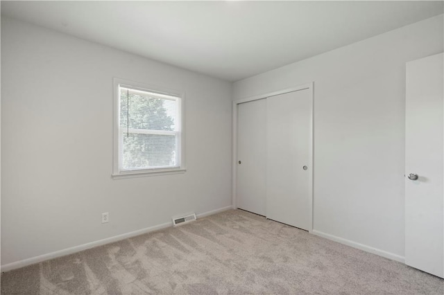 unfurnished bedroom featuring visible vents, baseboards, a closet, and light carpet