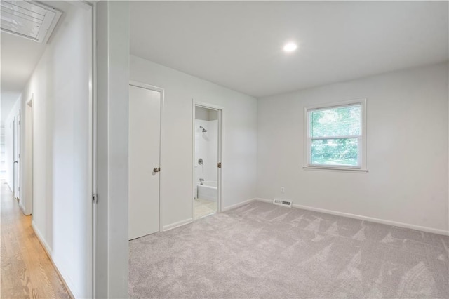 unfurnished bedroom featuring light carpet, attic access, baseboards, ensuite bathroom, and visible vents
