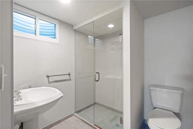 bathroom featuring tile patterned flooring, toilet, baseboards, a shower stall, and a sink