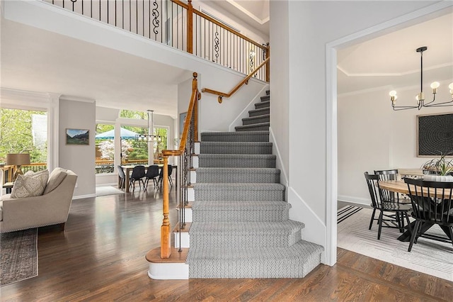 stairs with a chandelier, wood finished floors, baseboards, and ornamental molding