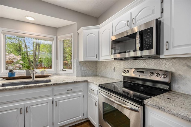 kitchen with stainless steel appliances, a sink, white cabinetry, backsplash, and light stone counters