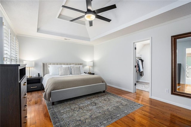 bedroom with a tray ceiling, wood finished floors, baseboards, a walk in closet, and ornamental molding