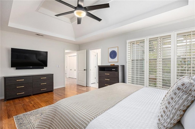 bedroom featuring a tray ceiling, wood finished floors, baseboards, crown molding, and a ceiling fan