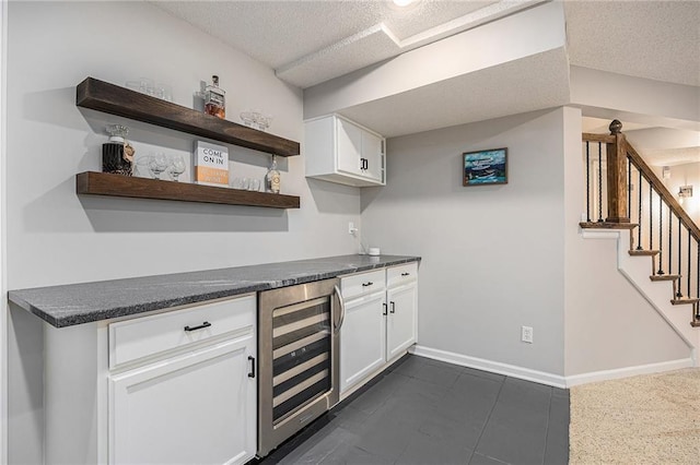 indoor bar featuring wine cooler, a textured ceiling, stairs, baseboards, and dark tile patterned floors