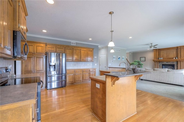 812 SW Stablewood Cir, Lees Summit, MO 64081 - kitchen featuring stainless steel appliances, a glass covered fireplace, crown molding, brown cabinets, and light wood-style floors