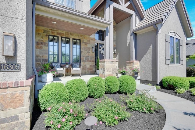property entrance featuring covered porch, stone siding, and stucco siding