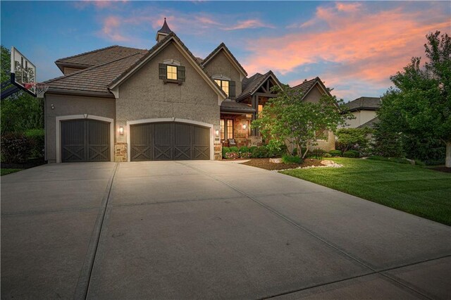view of front of property with driveway, a yard, stucco siding, an attached garage, and a tiled roof