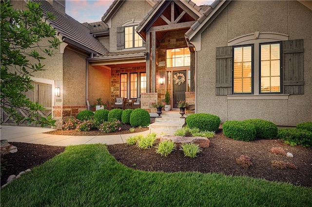 view of exterior entry with stone siding, a porch, stucco siding, and a tiled roof