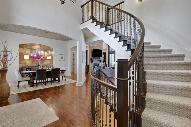 16305 Flint St, Overland Park, KS 66221 - staircase with arched walkways, a chandelier, wood finished floors, a stone fireplace, and a towering ceiling