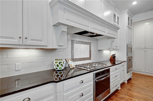 16305 Flint St, Overland Park, KS 66221 - kitchen featuring appliances with stainless steel finishes, dark countertops, white cabinets, decorative backsplash, and light wood-style flooring