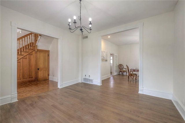 unfurnished dining area with visible vents, wood finished floors, an inviting chandelier, and stairway