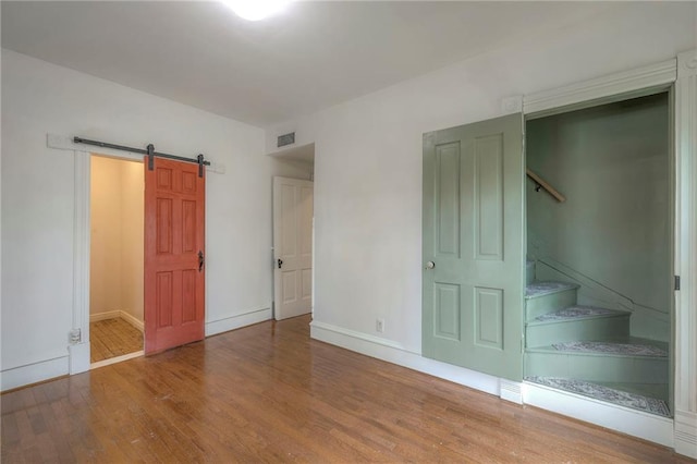 unfurnished bedroom featuring a barn door, visible vents, wood finished floors, and baseboards