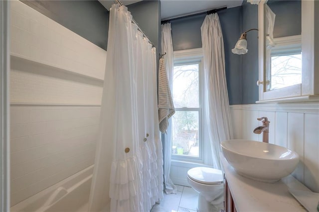 bathroom featuring shower / bath combo, a healthy amount of sunlight, toilet, and wainscoting