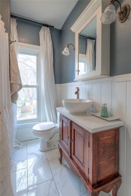 bathroom with toilet, vanity, a wainscoted wall, and marble finish floor