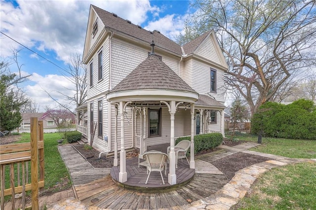 view of front facade featuring a front yard, a wooden deck, a shingled roof, and fence