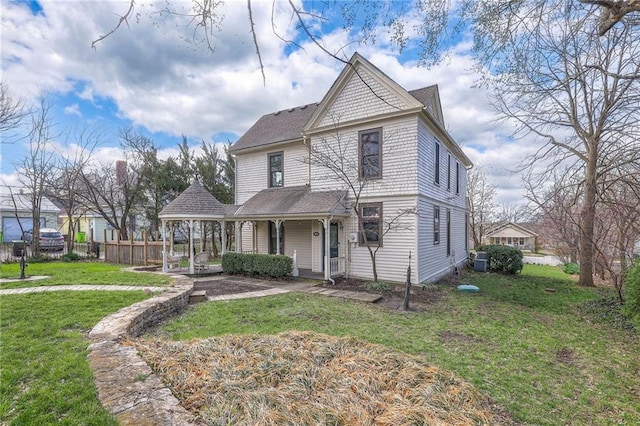 victorian-style house featuring central AC, fence, a front yard, and roof with shingles