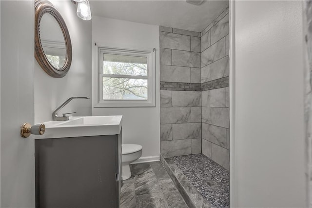 full bathroom featuring a tile shower, marble finish floor, toilet, vanity, and baseboards