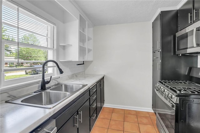 kitchen with appliances with stainless steel finishes, open shelves, a sink, dark cabinets, and light tile patterned flooring
