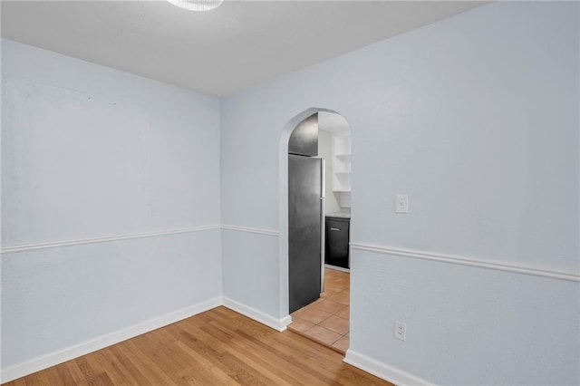 empty room featuring arched walkways, baseboards, and light wood-style flooring