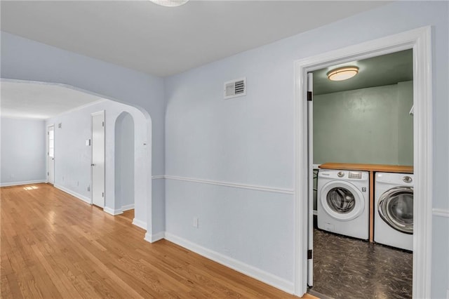 clothes washing area with independent washer and dryer, laundry area, arched walkways, wood finished floors, and visible vents