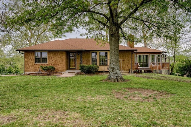 ranch-style house featuring brick siding, a chimney, a front yard, and a wooden deck