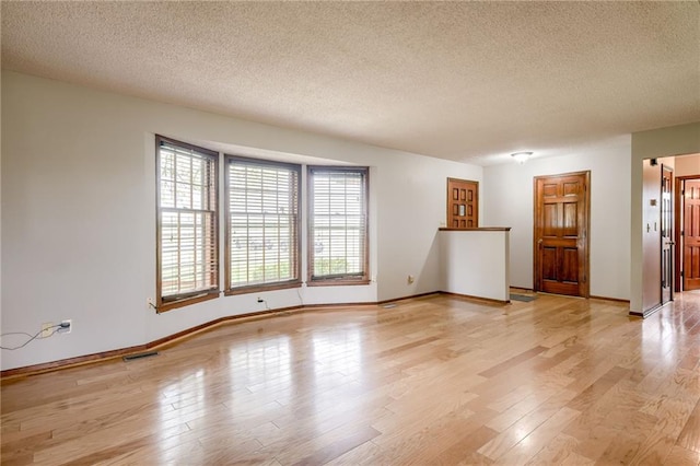 empty room featuring light wood-style floors, baseboards, and a textured ceiling