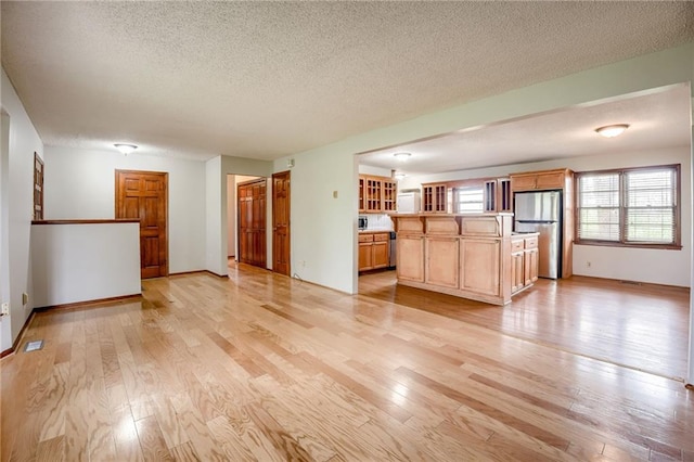 unfurnished living room featuring baseboards, light wood-style flooring, and a textured ceiling