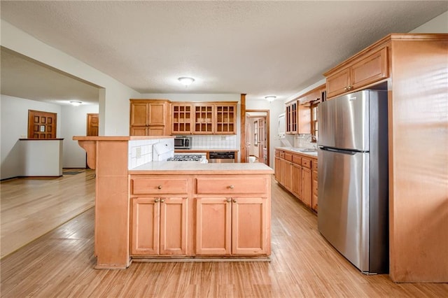kitchen with glass insert cabinets, light countertops, light wood-style flooring, backsplash, and stainless steel appliances