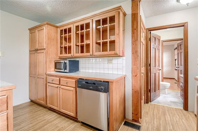 kitchen with appliances with stainless steel finishes, light countertops, a textured ceiling, light wood-style flooring, and tasteful backsplash