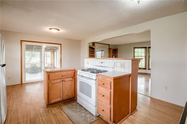kitchen featuring a textured ceiling, light wood-type flooring, light countertops, white gas range oven, and open floor plan