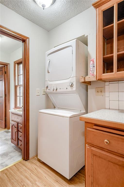 clothes washing area featuring light wood-style floors, a textured ceiling, stacked washer and clothes dryer, and cabinet space
