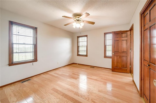interior space featuring ceiling fan, a textured ceiling, visible vents, light wood-type flooring, and baseboards