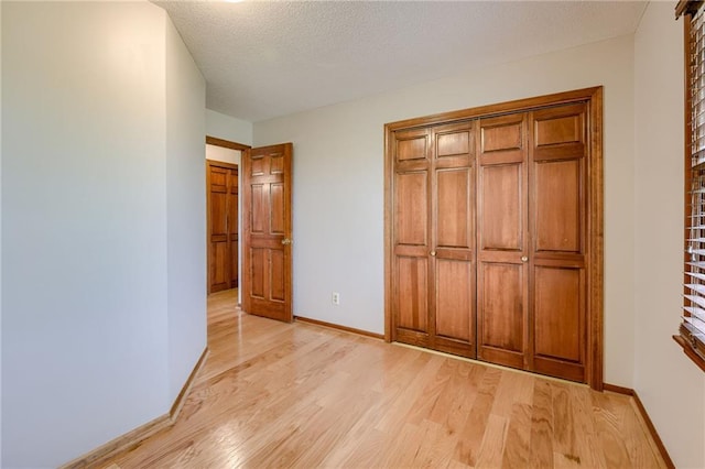 unfurnished bedroom with a textured ceiling, baseboards, and light wood finished floors