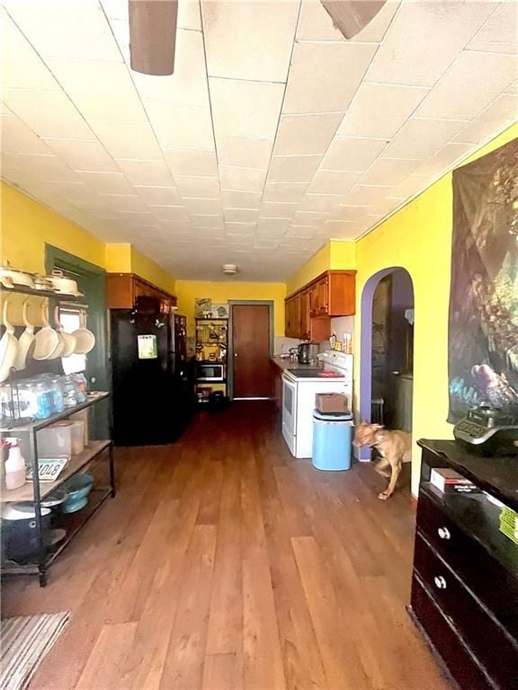 kitchen with brown cabinets, white range with electric stovetop, freestanding refrigerator, arched walkways, and dark wood finished floors