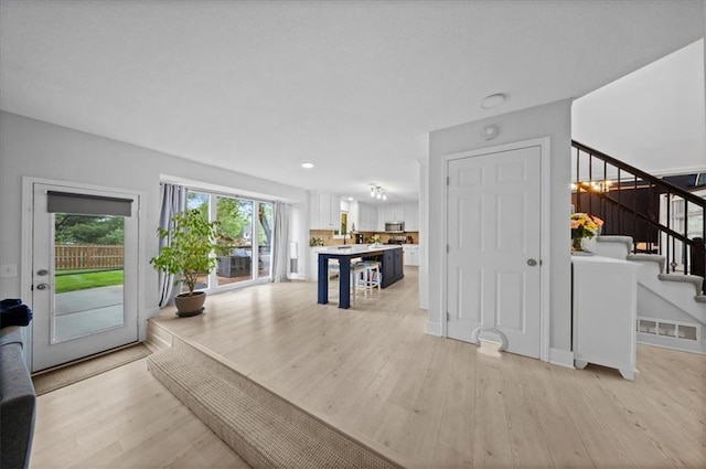 unfurnished living room with recessed lighting, light wood finished floors, and stairs