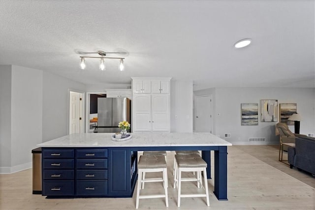 kitchen with blue cabinets, baseboards, white cabinets, freestanding refrigerator, and light wood-style floors