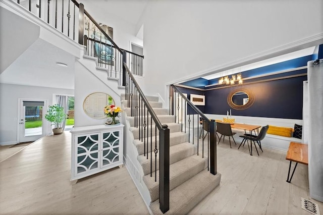 staircase with visible vents, a towering ceiling, wood finished floors, baseboards, and an inviting chandelier