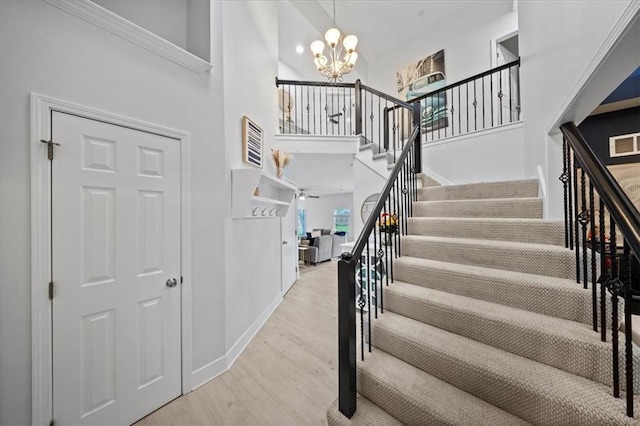 staircase with visible vents, a towering ceiling, wood finished floors, baseboards, and a chandelier