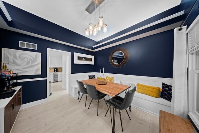 dining room featuring visible vents, wainscoting, a raised ceiling, light wood finished floors, and beverage cooler