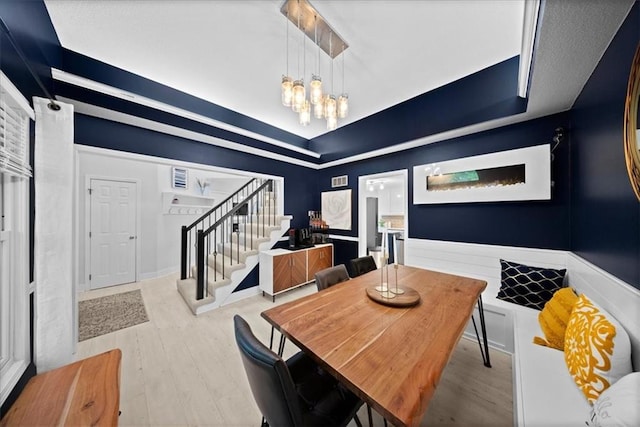 dining space with stairway, a raised ceiling, an inviting chandelier, and wood finished floors