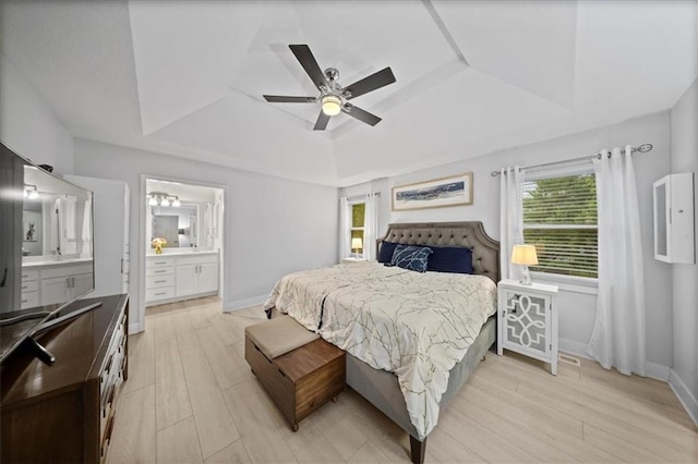 bedroom with a raised ceiling, ensuite bathroom, baseboards, and light wood-type flooring